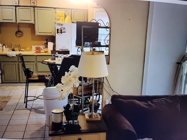 kitchen featuring white refrigerator with ice dispenser, sink, green cabinets, and light tile patterned floors