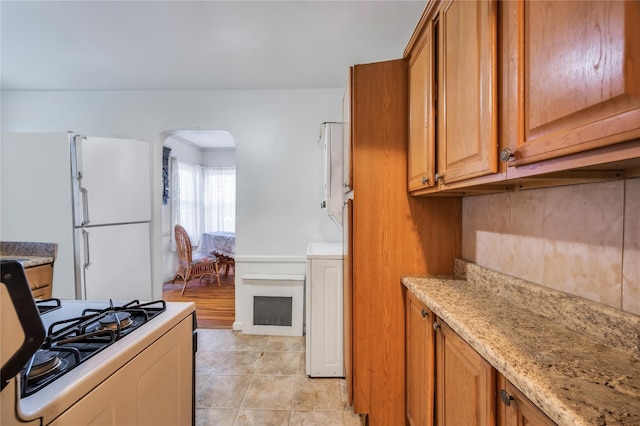 kitchen featuring range with gas cooktop, backsplash, white refrigerator, light tile patterned floors, and light stone counters