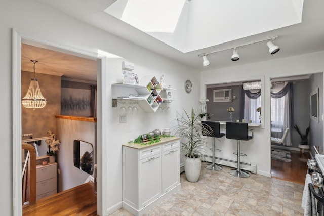 kitchen featuring baseboard heating, white cabinetry, a skylight, a wall unit AC, and decorative light fixtures