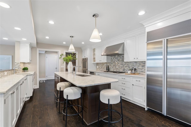 kitchen featuring stainless steel appliances, a breakfast bar, dark wood-style flooring, white cabinetry, and wall chimney exhaust hood