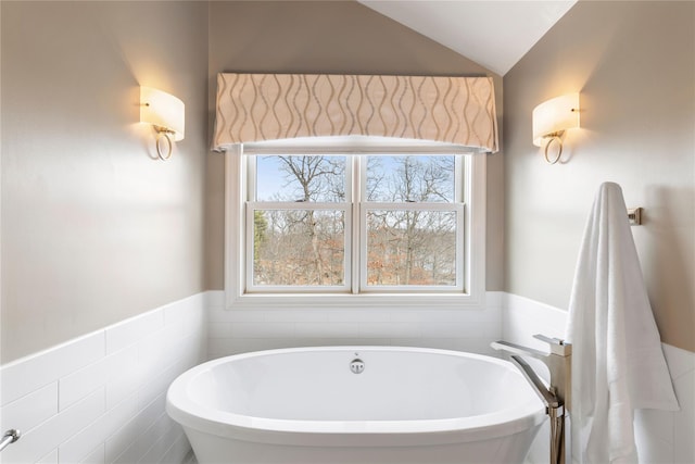 bathroom featuring a freestanding tub, wainscoting, vaulted ceiling, and tile walls