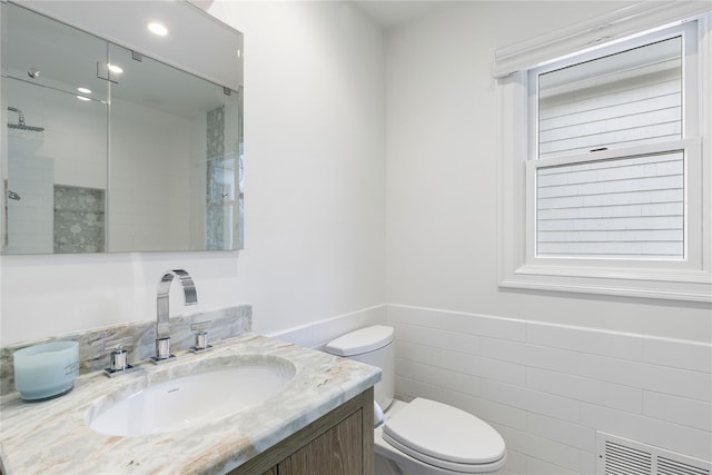 full bathroom featuring visible vents, toilet, vanity, a shower stall, and tile walls