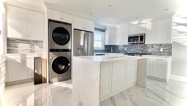 kitchen featuring appliances with stainless steel finishes, white cabinetry, a center island, stacked washer and clothes dryer, and tasteful backsplash