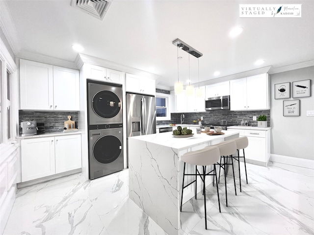 kitchen featuring a kitchen island, pendant lighting, white cabinetry, stacked washer and clothes dryer, and stainless steel appliances