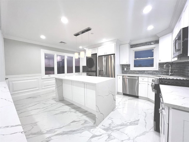 kitchen featuring stacked washing maching and dryer, a kitchen island, appliances with stainless steel finishes, white cabinets, and hanging light fixtures