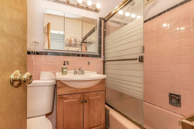 full bathroom featuring vanity, toilet, combined bath / shower with glass door, and tile walls