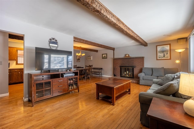 living room featuring beamed ceiling, a brick fireplace, light hardwood / wood-style flooring, and a notable chandelier