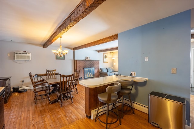 interior space featuring pendant lighting, a wall mounted air conditioner, light hardwood / wood-style floors, kitchen peninsula, and beam ceiling