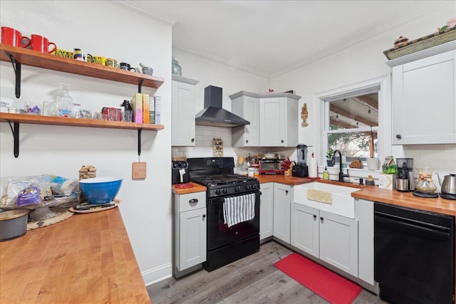 kitchen with sink, butcher block counters, ornamental molding, black appliances, and wall chimney exhaust hood