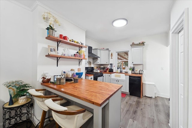 kitchen featuring wall chimney exhaust hood, butcher block counters, sink, a breakfast bar area, and black appliances