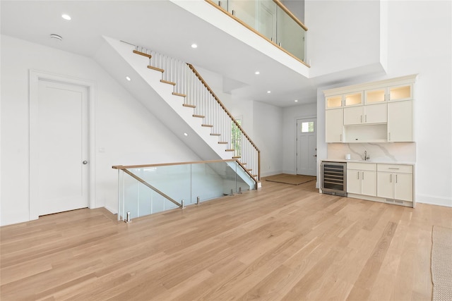 unfurnished living room featuring a towering ceiling, light hardwood / wood-style flooring, wet bar, and beverage cooler