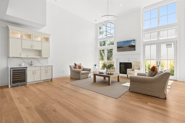 living room with wine cooler, indoor wet bar, light hardwood / wood-style flooring, a fireplace, and a high ceiling