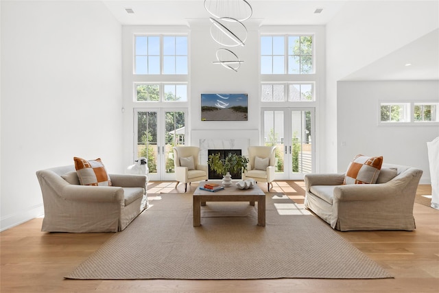 living room with a high end fireplace, light hardwood / wood-style flooring, french doors, and a wealth of natural light