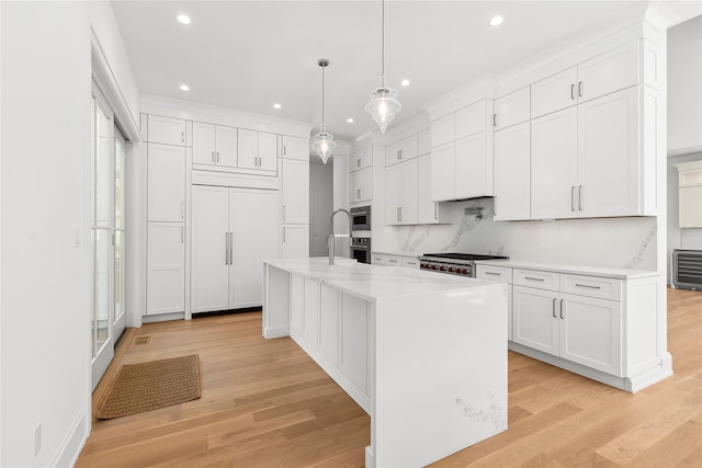 kitchen featuring light wood-type flooring, pendant lighting, light stone countertops, a kitchen island with sink, and white cabinets