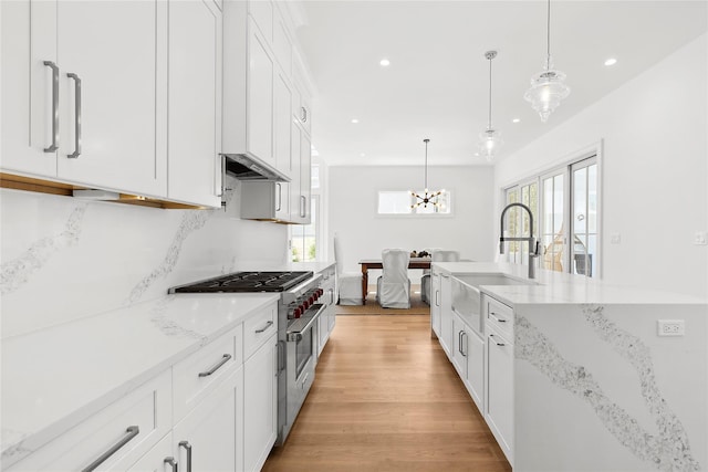 kitchen with white cabinetry, sink, hanging light fixtures, and high end stove