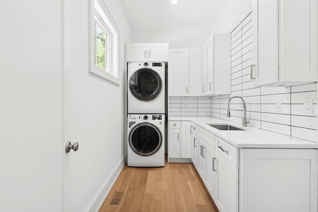 washroom featuring cabinets, stacked washer / drying machine, sink, and light wood-type flooring