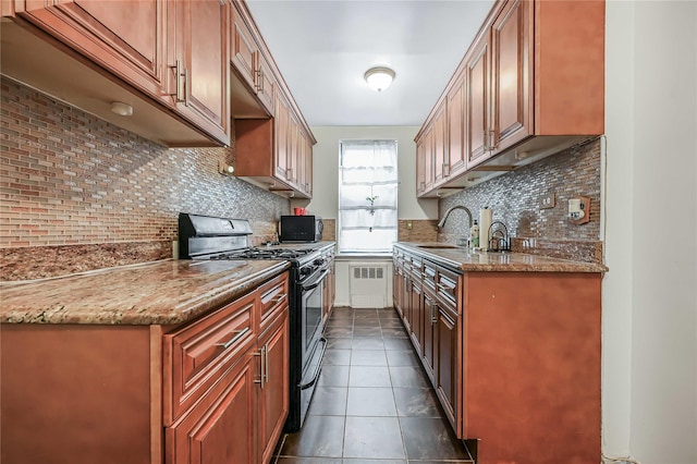 kitchen featuring radiator heating unit, sink, backsplash, gas range, and light stone countertops