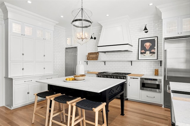 kitchen featuring premium range hood, white cabinetry, hanging light fixtures, ornamental molding, and high end appliances