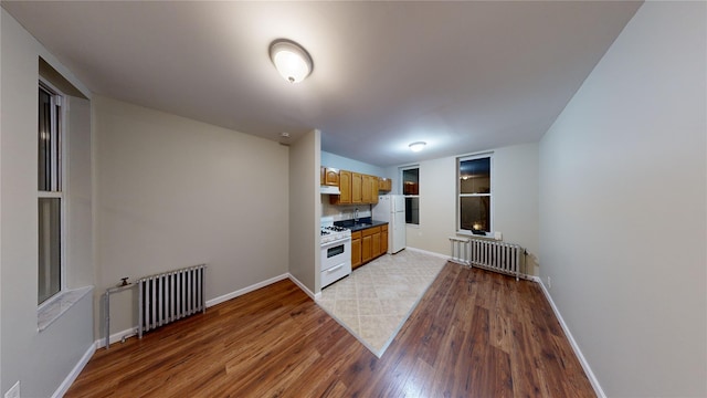 kitchen featuring white appliances, light brown cabinetry, radiator, and hardwood / wood-style floors