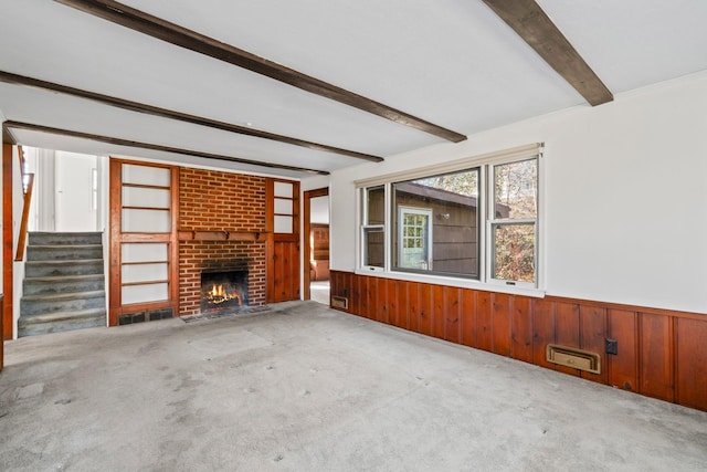 unfurnished living room with stairs, beam ceiling, carpet, and wainscoting