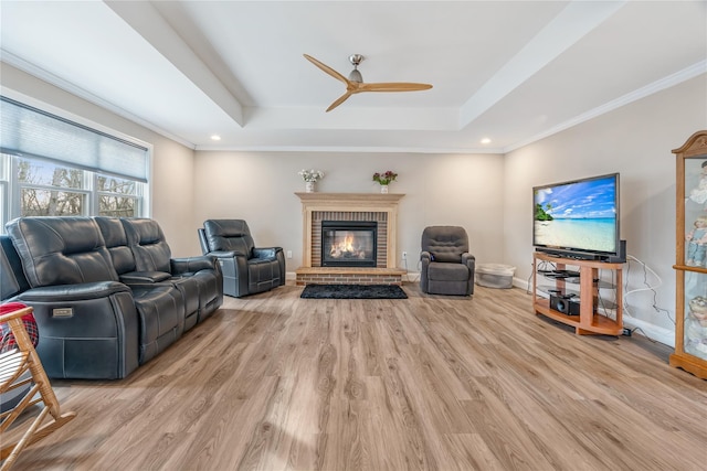 living room featuring crown molding, a fireplace, a tray ceiling, and light hardwood / wood-style floors