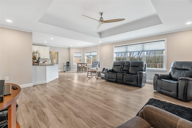 living room with a tray ceiling, light hardwood / wood-style flooring, ornamental molding, and ceiling fan