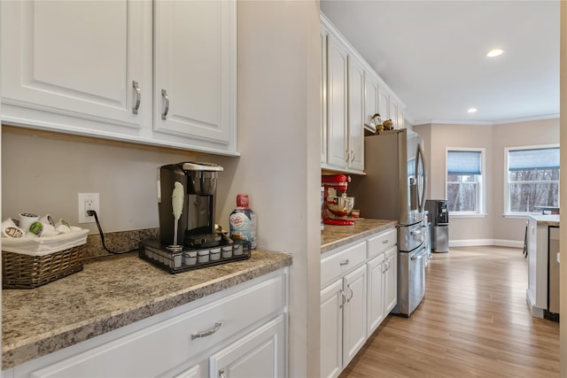 kitchen with white cabinetry, light hardwood / wood-style flooring, ornamental molding, stainless steel fridge, and light stone countertops