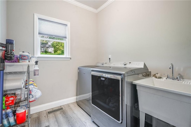 laundry room featuring sink, crown molding, washing machine and clothes dryer, and light wood-type flooring