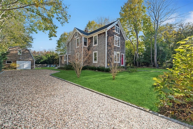 view of front of property with gravel driveway, a detached garage, a chimney, a front yard, and an outdoor structure