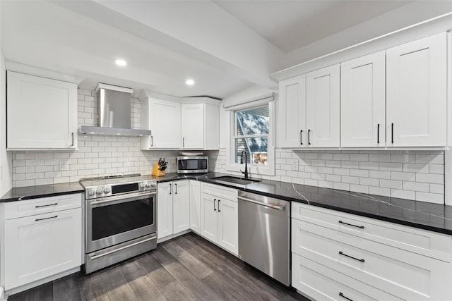 kitchen featuring tasteful backsplash, wall chimney exhaust hood, appliances with stainless steel finishes, dark wood-style flooring, and a sink