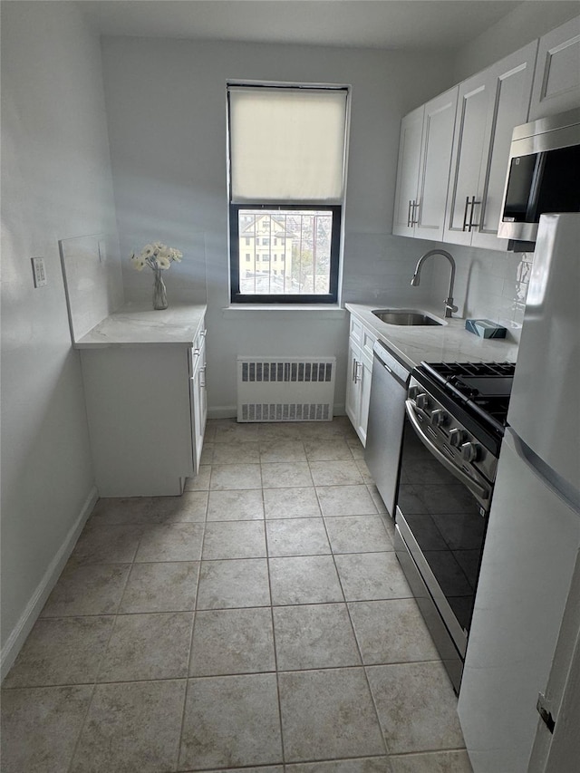 kitchen with light tile patterned flooring, sink, appliances with stainless steel finishes, radiator heating unit, and white cabinets