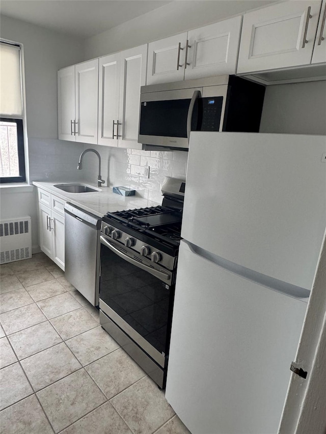 kitchen with appliances with stainless steel finishes, sink, radiator heating unit, and white cabinets