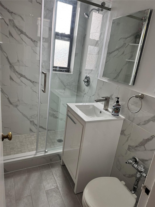 bathroom with vanity, toilet, a shower with door, and tile walls