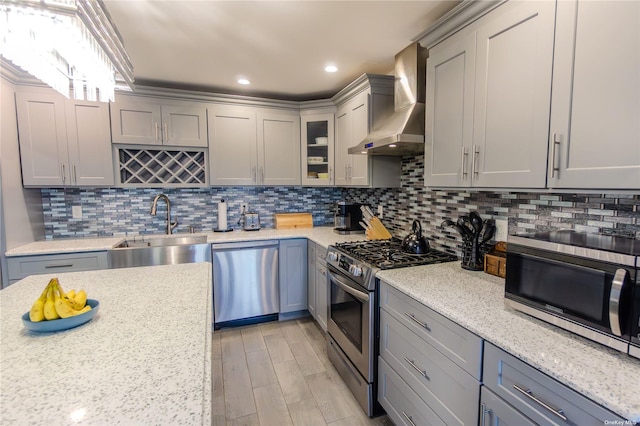 kitchen featuring wall chimney range hood, sink, appliances with stainless steel finishes, light stone countertops, and decorative backsplash