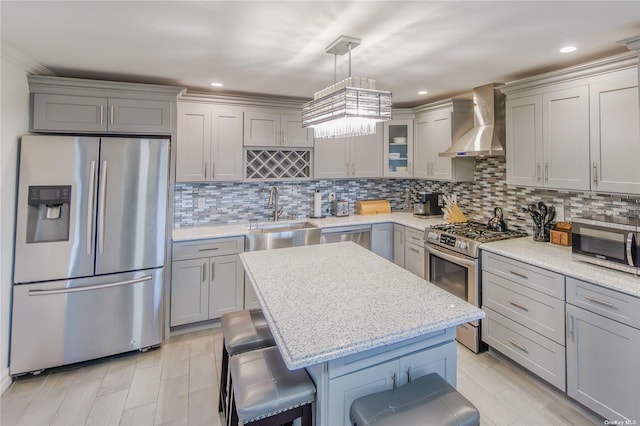 kitchen with sink, a kitchen breakfast bar, hanging light fixtures, stainless steel appliances, and wall chimney exhaust hood