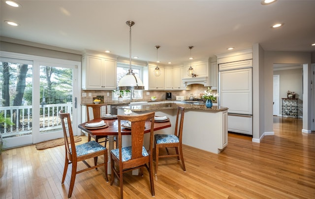 kitchen with pendant lighting, white cabinetry, a kitchen island, decorative backsplash, and dark stone counters