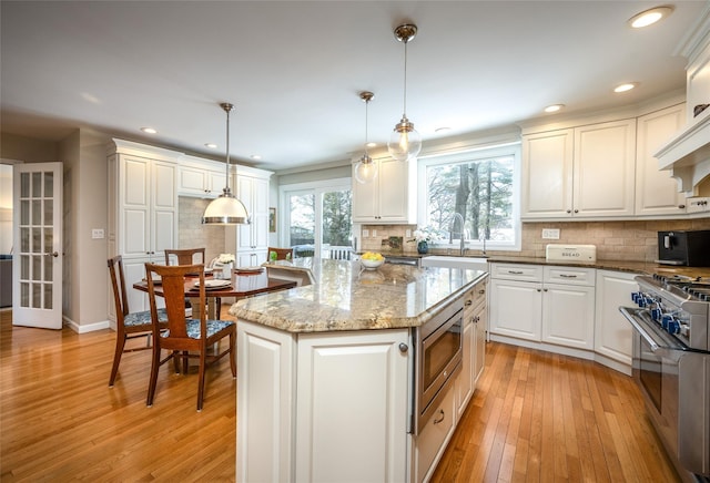 kitchen with decorative light fixtures, a center island, white cabinets, and appliances with stainless steel finishes