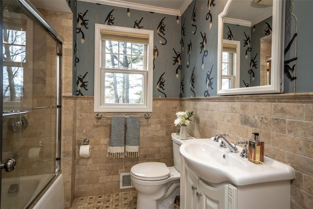 full bathroom with tile walls, shower / bath combination with glass door, vanity, toilet, and crown molding