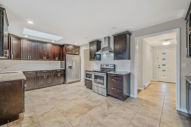 kitchen with light stone counters, wall chimney range hood, a skylight, and appliances with stainless steel finishes