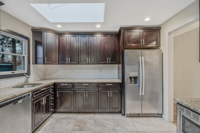 kitchen with dark brown cabinetry, appliances with stainless steel finishes, a skylight, and sink