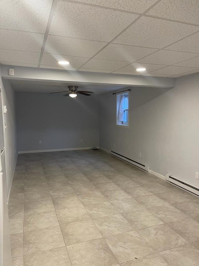 basement featuring a paneled ceiling, ceiling fan, and baseboard heating