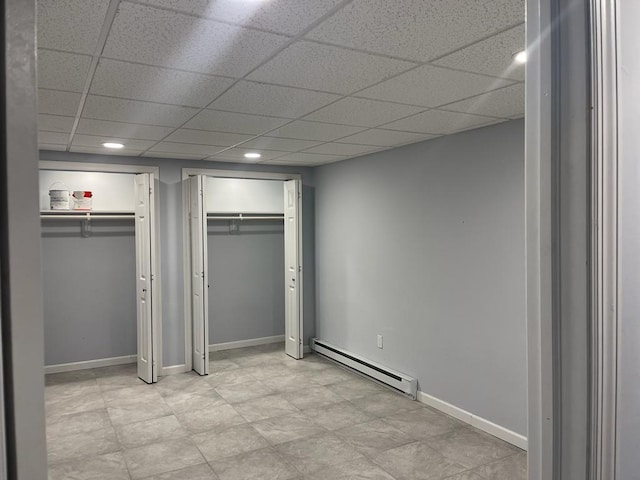 unfurnished bedroom featuring baseboard heating, a paneled ceiling, and two closets