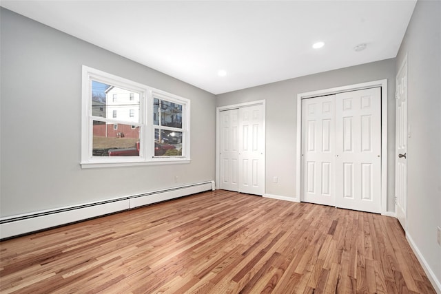 unfurnished bedroom featuring a baseboard heating unit, light hardwood / wood-style floors, and two closets