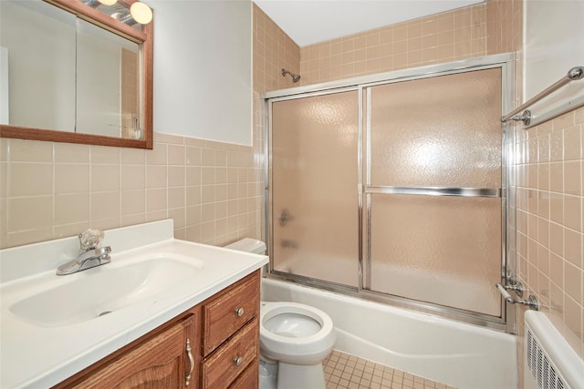 full bathroom featuring radiator, tile walls, tile patterned flooring, bath / shower combo with glass door, and vanity