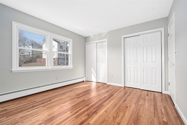 unfurnished bedroom featuring multiple closets, baseboard heating, and light hardwood / wood-style flooring