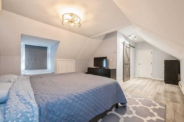 bedroom featuring a barn door, lofted ceiling, and light hardwood / wood-style floors