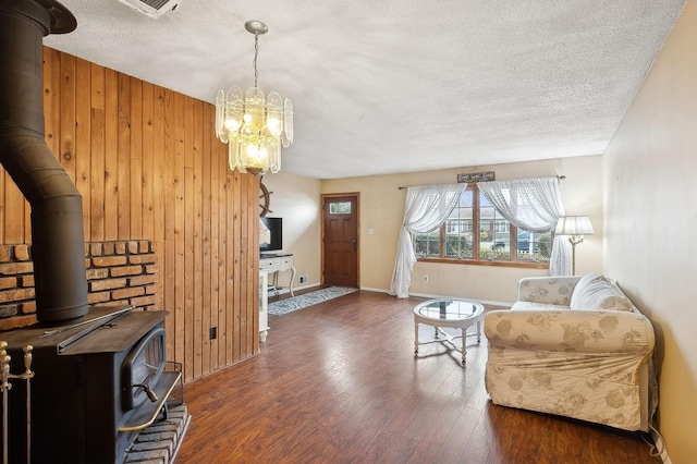 living room featuring dark wood-type flooring, wooden walls, a textured ceiling, and a wood stove