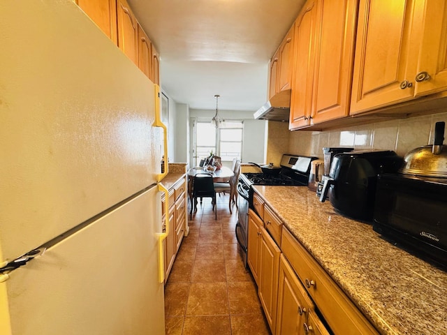 kitchen featuring backsplash, fridge, stainless steel range with gas stovetop, dark tile patterned flooring, and decorative light fixtures