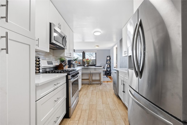 kitchen with tasteful backsplash, stainless steel appliances, white cabinets, and light wood-type flooring