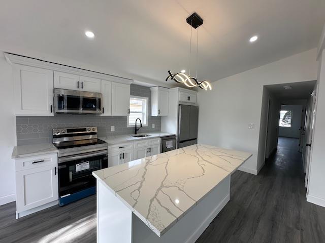 kitchen featuring a kitchen island, white cabinetry, appliances with stainless steel finishes, and decorative light fixtures